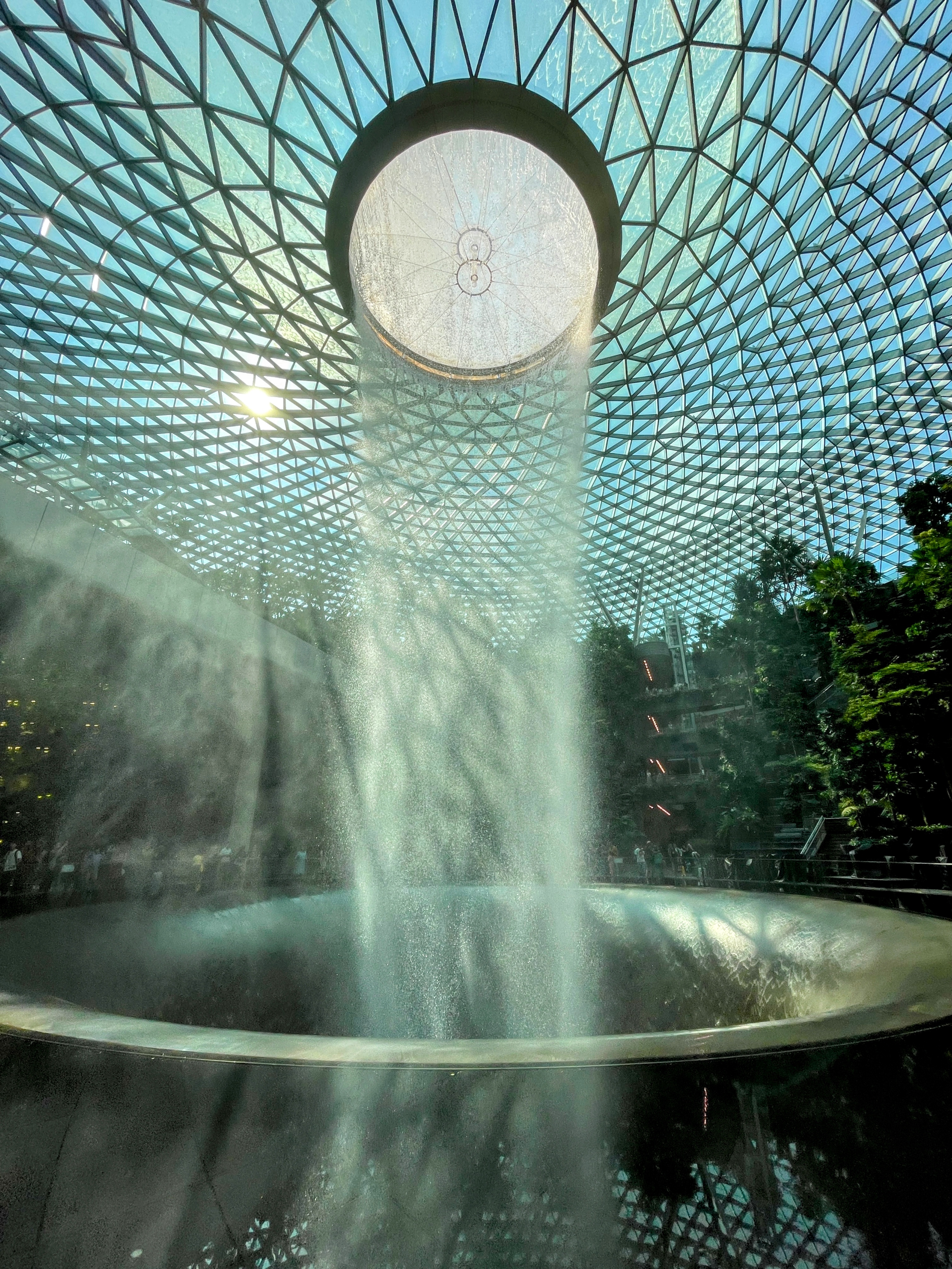 The Rain Vortex indoor waterfall at Jewel Changi Airport, cascading under the geometric glass dome with sunlight filtering through.